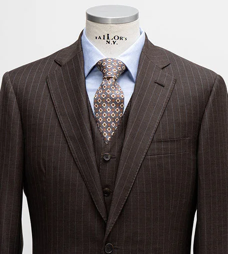 Close-up of brown blazer with thin vertical stripes, light shirt, diamond pattern tie, and matching vest.