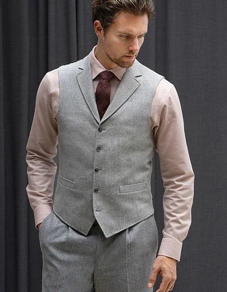 Male model in grey two-piece suit with red shirt and burgundy tie standing in front of grey curtain.