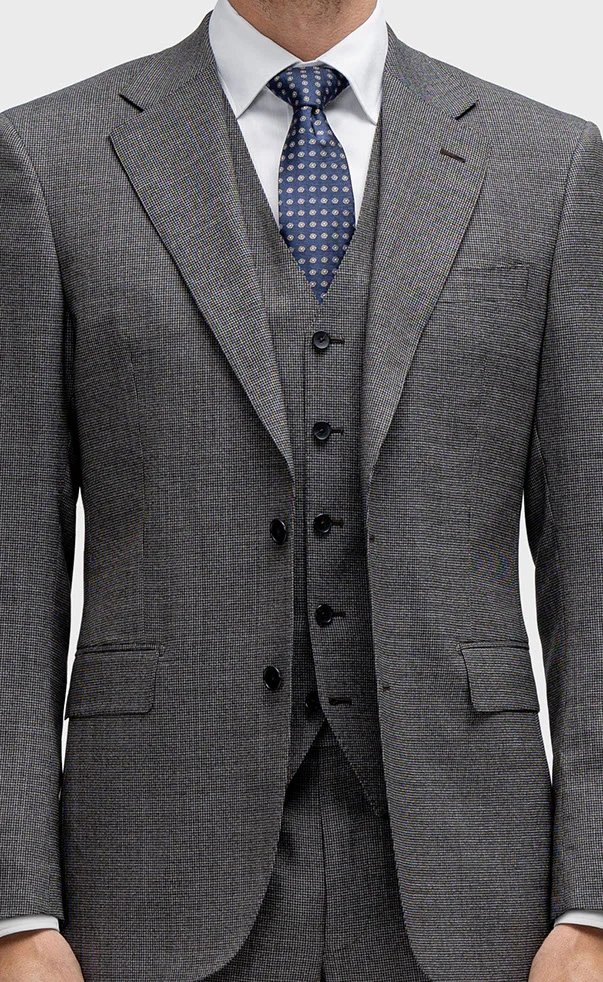 Close-up of model in dark gray textured suit, matching vest, white shirt, and navy polka dot tie.