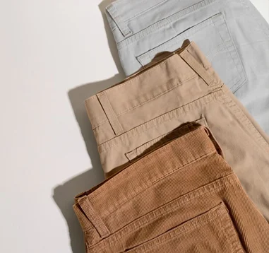 Stack of folded pants in light beige, sand, and camel colors representing casual and elegant menswear.