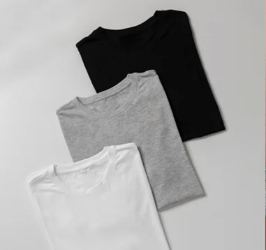 Stack of folded white, gray, and black basic T-shirts representing minimalist and versatile style.